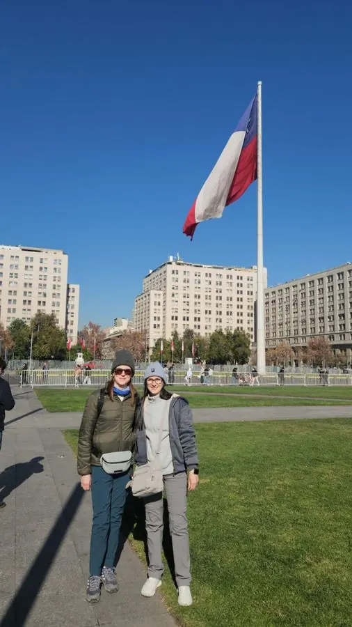 Two travelers in front of the giant Chilean flag by La Moneda Palace
