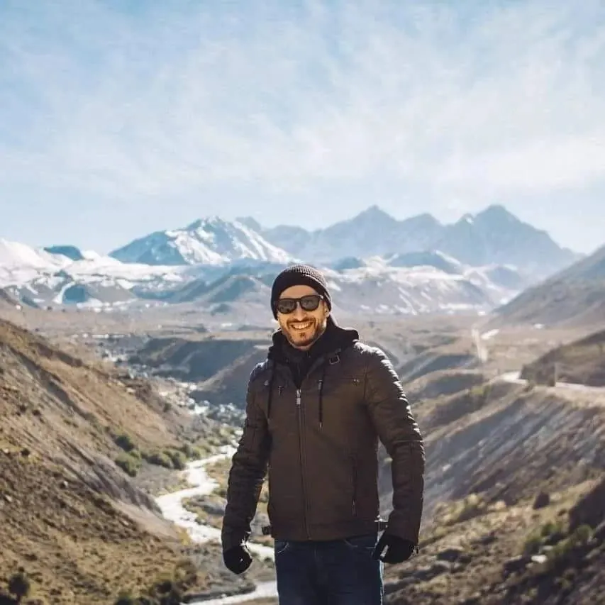 Traveler with the snow-capped Andes and a river behind, on the road to the high mountains