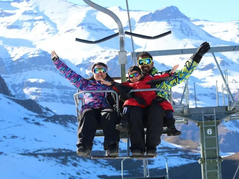 Family on a chairlift with snowy mountains behind, near Santiago, Chile